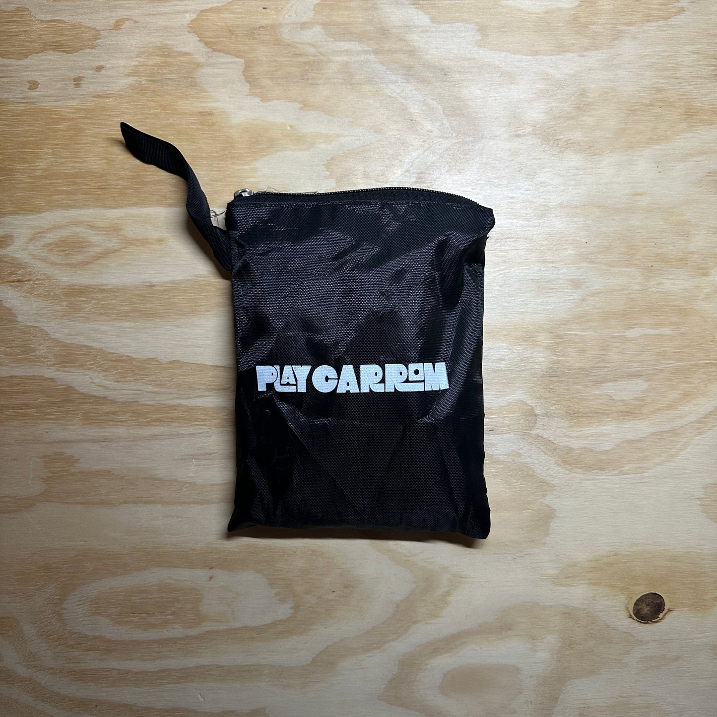 Black drawstring bag with 'Play Carrom' branding on a wooden surface